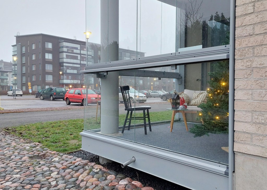 Näkymä parkkialueelle. Taustalla kerrostalo, etualalla parveke, jossa joulukuusi ja joulukoristeita. Kuva Päivi Leinonen